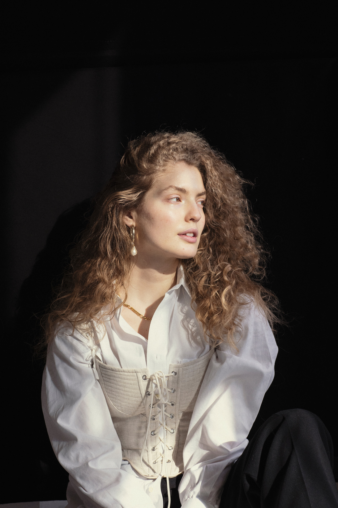 Fashionable young female model sitting in dark room and looking away